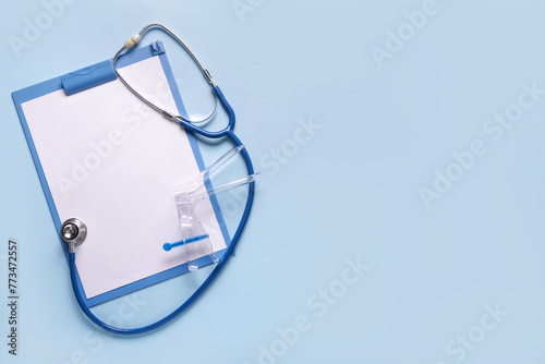 Clipboard with stethoscope and gynecological speculum on blue background
