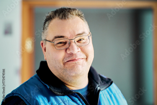 Sly smile of round faced European man over 40 wearing glasses.