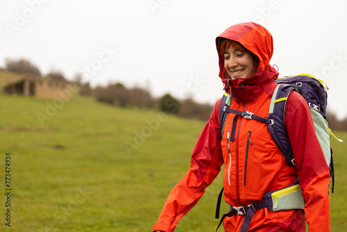 A woman wearing a red jacket and a backpack is walking in a field