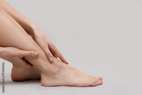 Woman suffering from leg pain on grey background, closeup. Space for text © New Africa