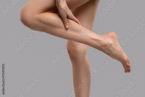 Woman suffering from leg pain on grey background, closeup © New Africa