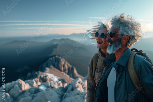 An senior couple stands triumphantly at the summit, enjoying the expansive mountain views at dawn, with a sense of peace and achievement.