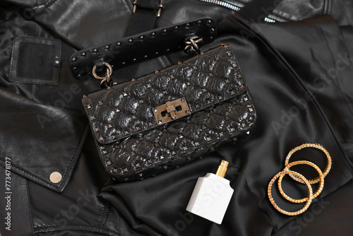 Leather bag, bottle of perfume and golden bracelets on black fabric, flat lay