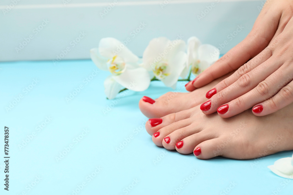 Woman with stylish red toenails after pedicure procedure and orchid flowers on light blue background, closeup. Space for text
