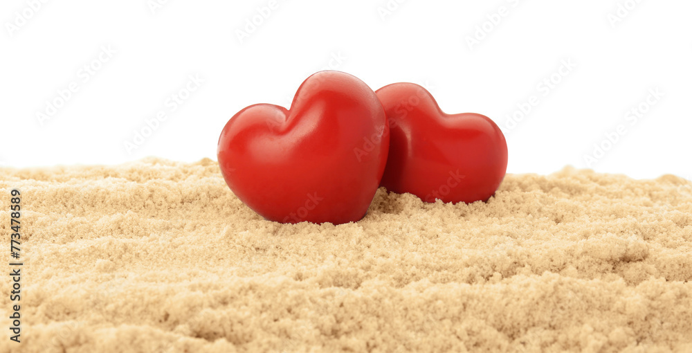 Fototapeta premium Honeymoon concept. Two red wooden hearts and sand isolated on white