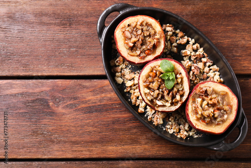 Tasty baked apples with nuts, honey and mint in baking dish on wooden table, top view. Space for text