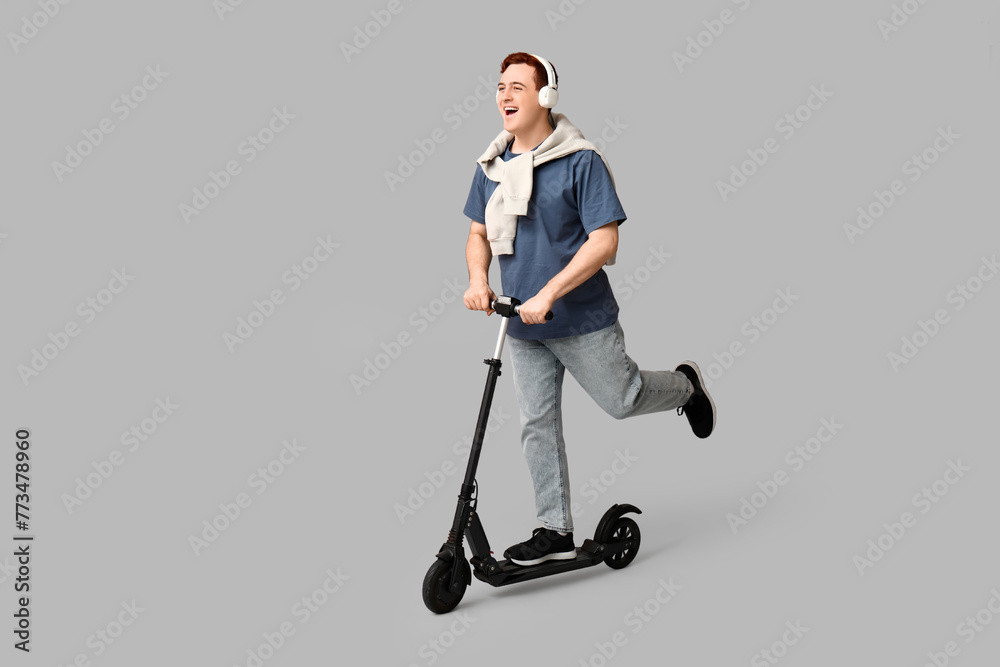Young man in headphones riding modern electric kick scooter on grey background Young man in headphones riding modern electric kick scooter on grey background