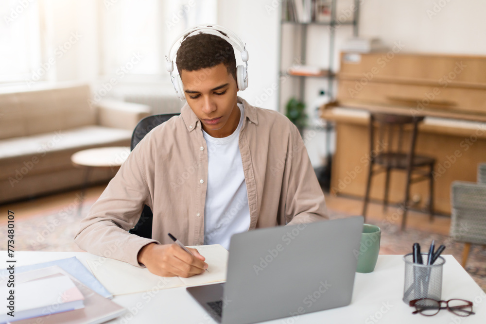 Fototapeta premium Man with headphones writing notes at desk