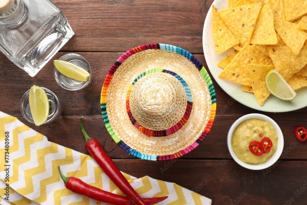 Mexican sombrero hat, tequila with lime, chili peppers, nachos chips and dip sauce on wooden table, flat lay Mexican sombrero hat, tequila with lime, chili peppers, nachos chips and dip sauce on wooden table, flat lay