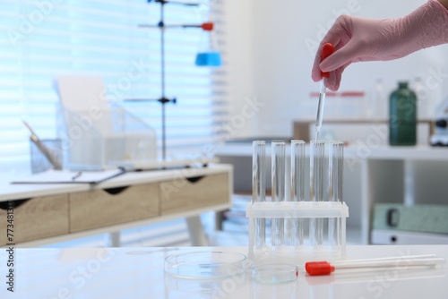 Laboratory analysis. Woman dripping liquid into test tubes at white table indoors  closeup