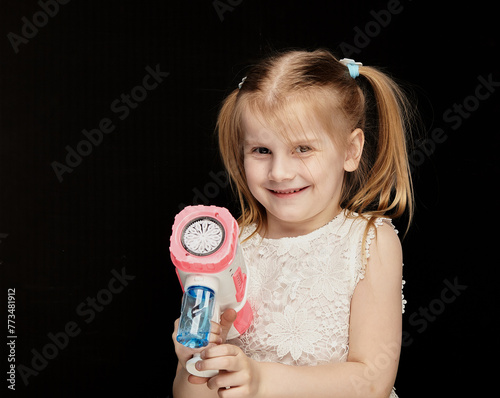 Child blonde girl 6 years old in a white dress on a dark background among air bubbles