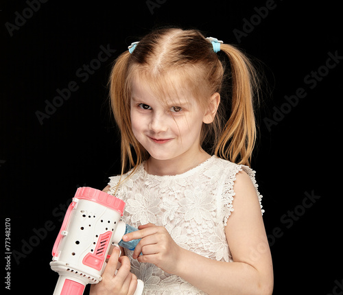 Child blonde girl 6 years old in a white dress on a dark background among air bubbles