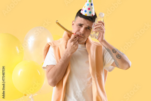 Young man with hangover and water bottle after Birthday party on yellow background