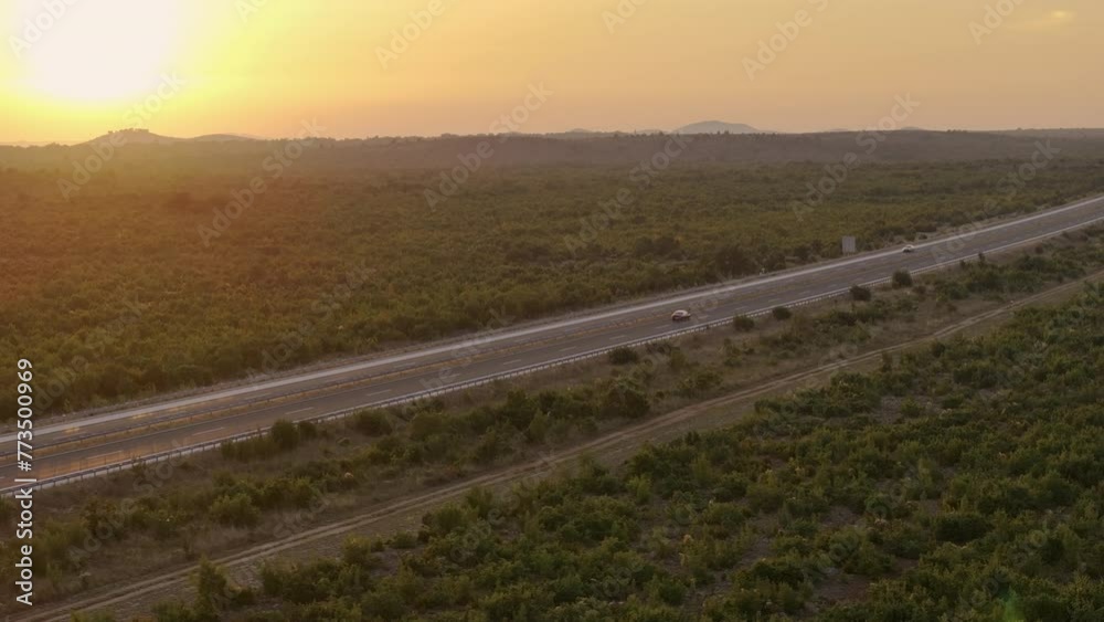 AERIAL: Beautiful summer evening sunbeams shine on the asphalt highway crossing the rural Croatia. Tourists drive their cars along the scenic freeway in the rural parts of coastal Croatia, Europe.