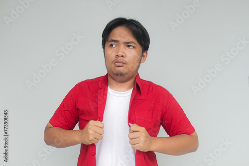 Portrait of a young Asian man in a red shirt with a cocky expression. Isolated in gray background.