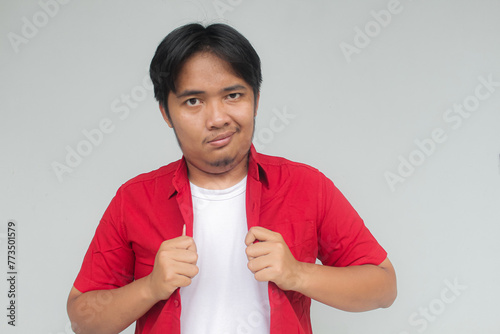 Portrait of a young Asian man in a red shirt with a cocky expression. Isolated in gray background. photo