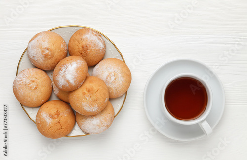 Round-shaped pastry, sprinkled with powdered sugar, on a plate and a cup of tea. view from above