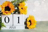 Canada Day. White wood calendar blocks with the date July 1st and beautiful sunflower bouquet with bokeh. Selective focus with blurred background. 
