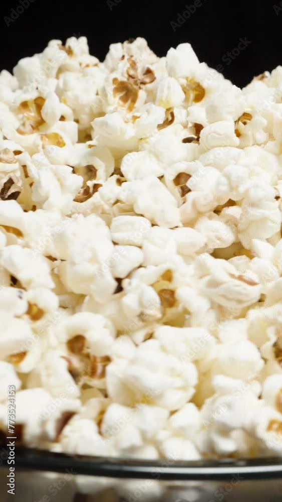 Vertical video. Popcorn is poured into a bowl with a heap. Rotation against a black background. Looping. Vertical video. Popcorn is poured into a bowl with a heap. Rotation against a black background. Looping.
