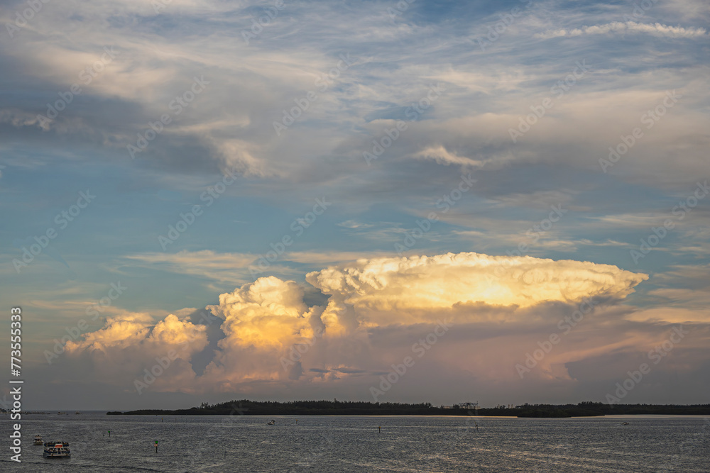 Miami, Florida, USA - July 29, 2023: Mushroom sunset cloud over Virginia Key island with moon far above in blue sky. Tour boat on bay. Wastewater treatment industrial complex