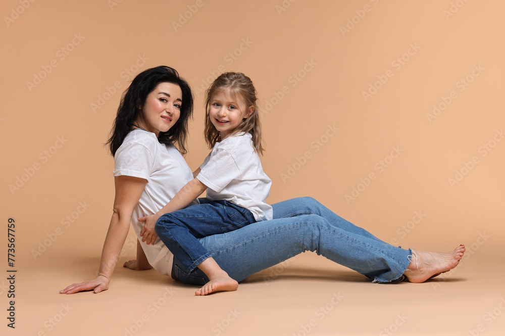 Beautiful mother with little daughter sitting on beige background Beautiful mother with little daughter sitting on beige background