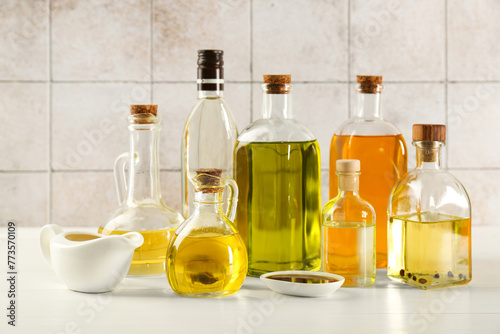 Vegetable fats. Different oils in glass bottles and dishware on white wooden table against tiled wall © New Africa