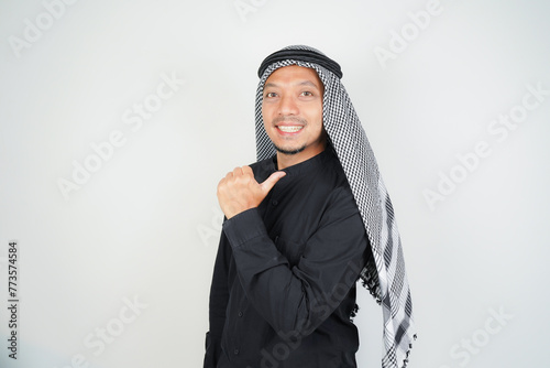Cheerful Asian Muslim man wearing Arab turban sorban pointing hand finger at empty space on isolated photo