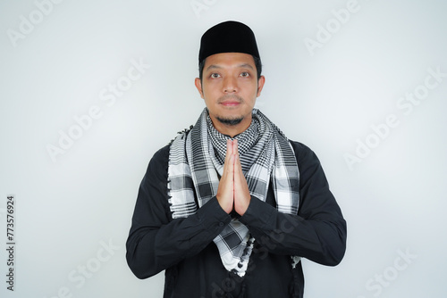 Happy smiling Asian Muslim man in Arabic turban sorban standing with Eid greeting gesture and welcoming Ramadan isolated background photo