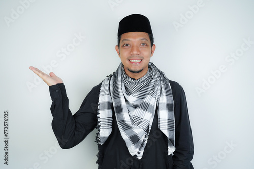 Cheerful handsome Asian Muslim man wearing Arab turban sorban pointing hand finger at empty space for advertising on isolated background photo