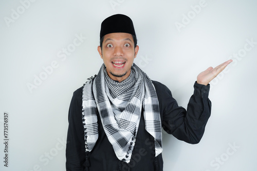 Cheerful handsome Asian Muslim man wearing Arab turban sorban pointing hand finger at empty space for advertising on isolated background photo