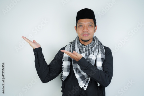 Cheerful handsome Asian Muslim man wearing Arab turban sorban pointing hand finger at empty space for advertising on isolated background photo