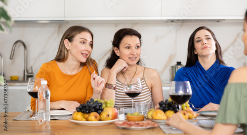 Female friends are sitting at table, chatting sweetly, discussing and telling news, sharing plans. Women celebrates housewarming party with relatives sisters.