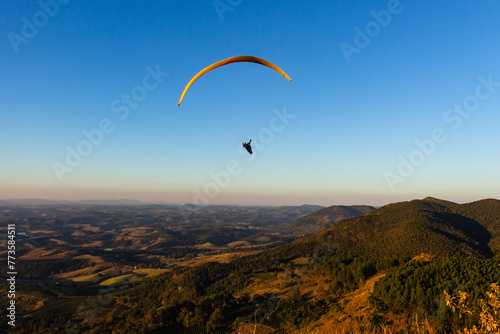 Paraglider na hora dourada - POÇOS DE CALDAS, MG, BRAZIL - JULY 22, 2023: Paraglider flying in the late afternoon with the sunlight making a beautiful gold color on the mountains.