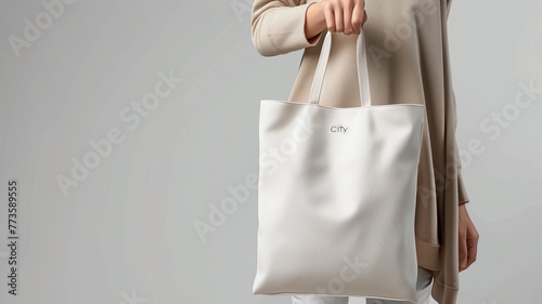 A mockup of a blank white tote bag held in a woman's hand, front view, mockup
