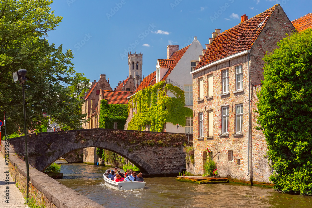 Fototapeta premium Tourists on a boat tour explore Medieval tower Belfort and Green canal, Groenerei, Bruges, Belgium