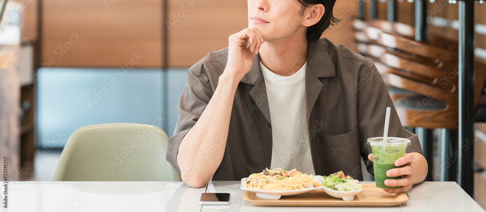 カフェでランチを食べながらグリーンスムージーを飲む若い男性（酵素・デトックス・食物繊維・健康食品）
