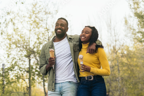 black couple eating ice cream while walking in a park