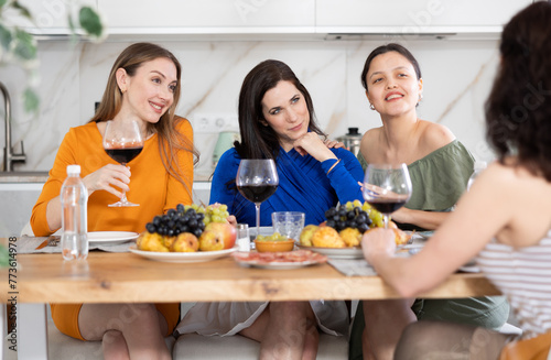 Girlfriends chatting and drinking wine at home party table in kitchen