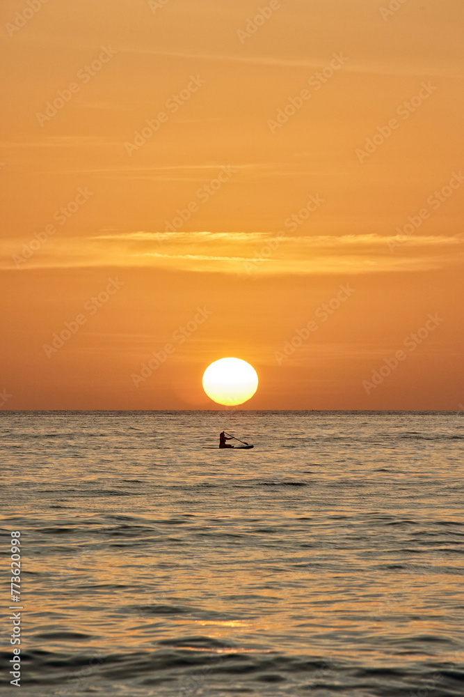 A girl with an oar on a SUP board floats on the sea against the backdrop of the setting sun