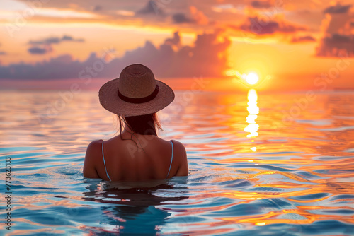 Woman wearing a hat on vacation relaxing in the ocean with the sunset on the horizon  serene summer reflection in the water