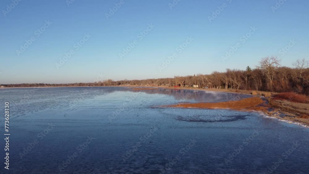 aerial pan out from sandy shore across partially frozen lake aerial pan out from sandy shore across partially frozen lake