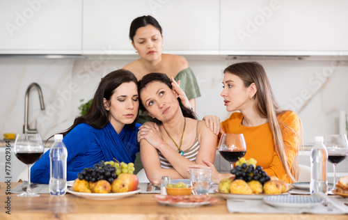 Frustrated and distressed Spanish woman sits in kitchen and complains to her female friends  talks about her difficulties at work  problems  vicissitudes. Women friends give advice  reassure  support