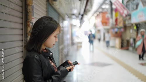 Slow-motion video of the face of an Okinawan woman in her 20s in winter clothes standing in a shopping street nead operating a smartphone on Kokusai Street in Naha City, Okinawa Prefecture 沖縄県那覇市の国際通り photo