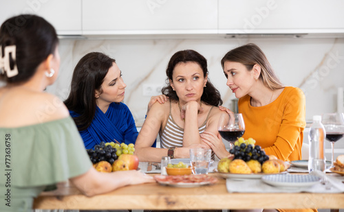 Group of besties gathered for intimate get-together at table with wine and light snacks, consoling woman after emotional upset, showcasing genuine care and attention