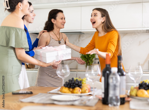 Girlfriends greet each other and give gift when meeting in kitchen..