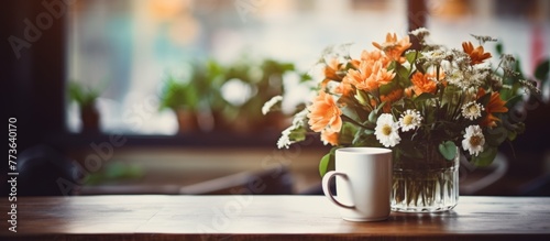 Colorful flowers arranged in a vase are placed next to a cup on a wooden table