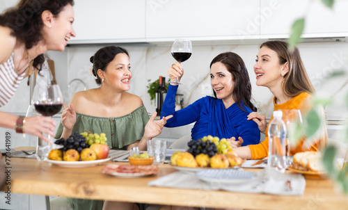 Girlfriends chatting and drinking wine at home party table in kitchen