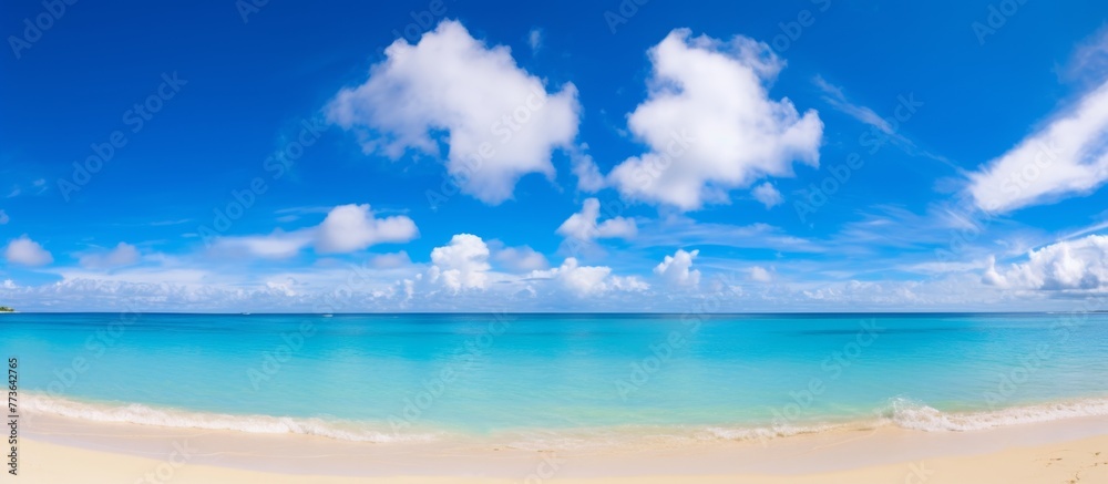 The serene beach offers a breathtaking view of the crystal clear blue ocean water and the white fluffy clouds in the sky