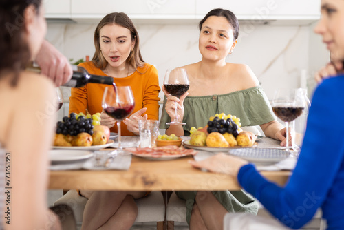 Girl are sitting at table with female friends, drinking wine and enjoying snacks, chatting merrily, raise glass to, celebrating important event.