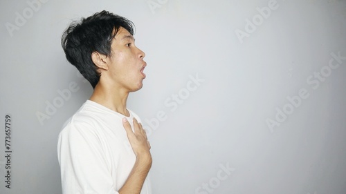 Side view of young Asian man in shock while holding his chest on an isolated white background